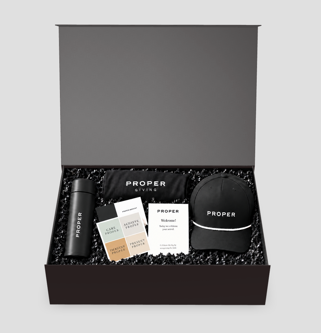Approved conceptual open-box composition with attached plain lid, PROPER bottle, cap, shirt, printed cards and black fill.